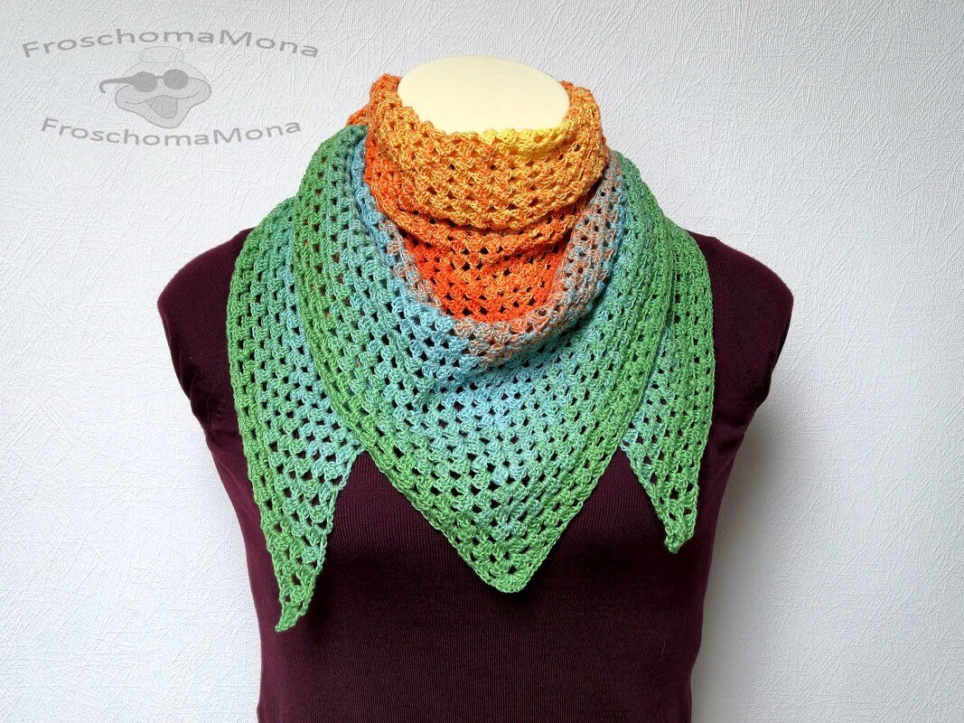 Gehäkeltes Dreieckstuch auf Schaufensterpuppe mit Farbverlauf von Orange über Blau zu Grün und offenem Lochmuster.