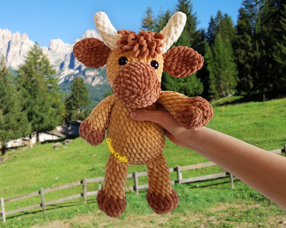 Hand holding a tan and brown crocheted amigurumi cow with ivory horns