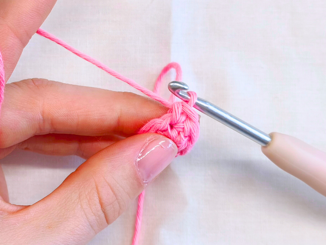 Hand hält pinkes Häkelgarn und Häkelnadel, eingeführt in eine rosa Häkelarbeit.
