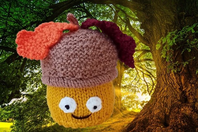 Knitted acorn plushie with purple-brown cap, orange and maroon leaves, and a yellow smiling body in a sunlit forest.